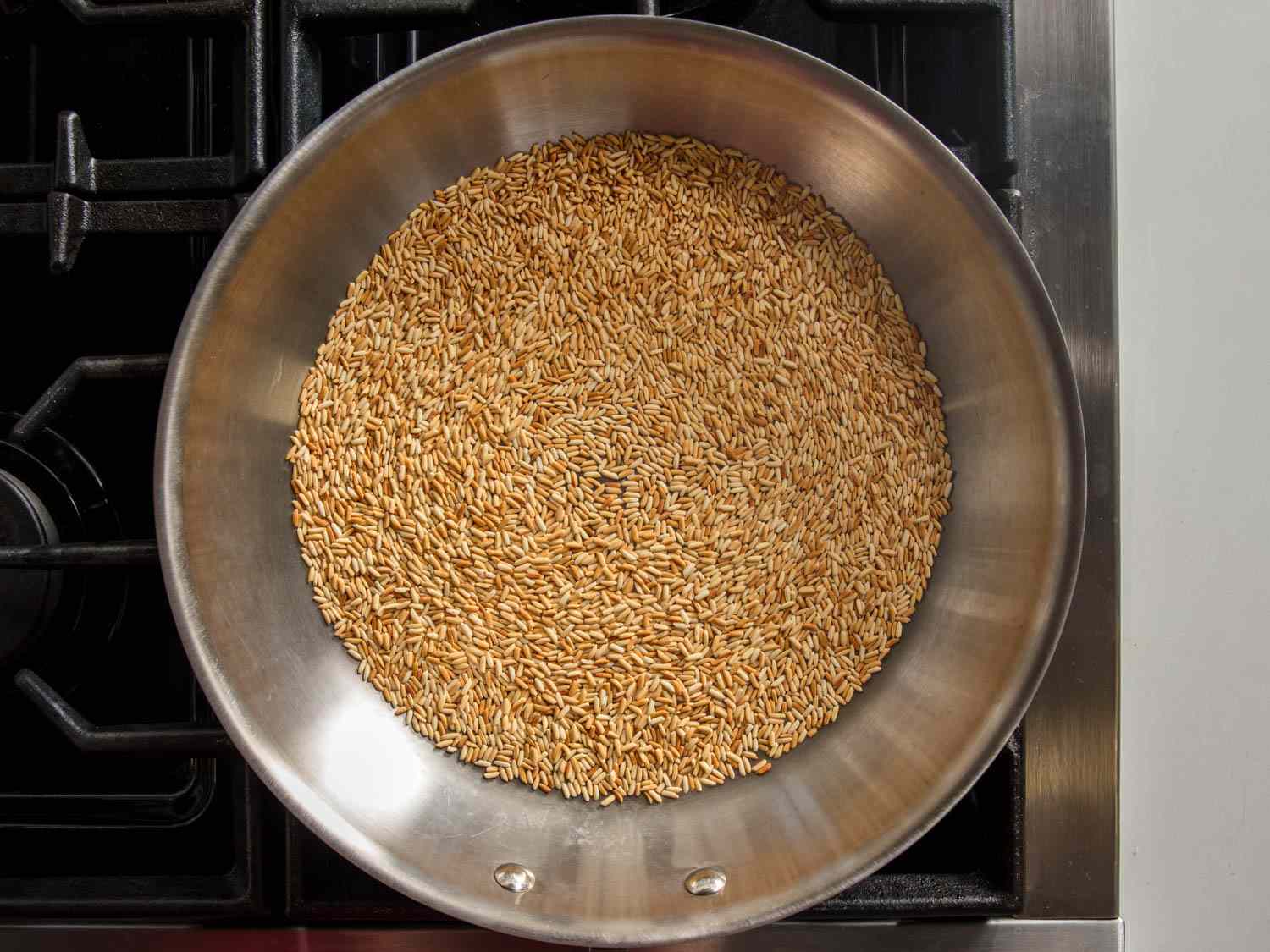 Brown rice being stirred in a saucepan with olive oil on a stovetop, showing the toasting step in progress