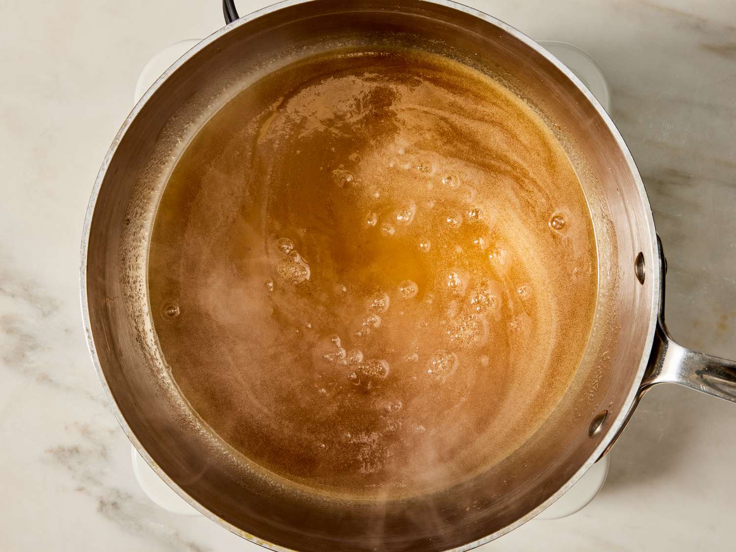 Brown sugar and butter melting together in a small saucepan while a whisk stirs on the stovetop