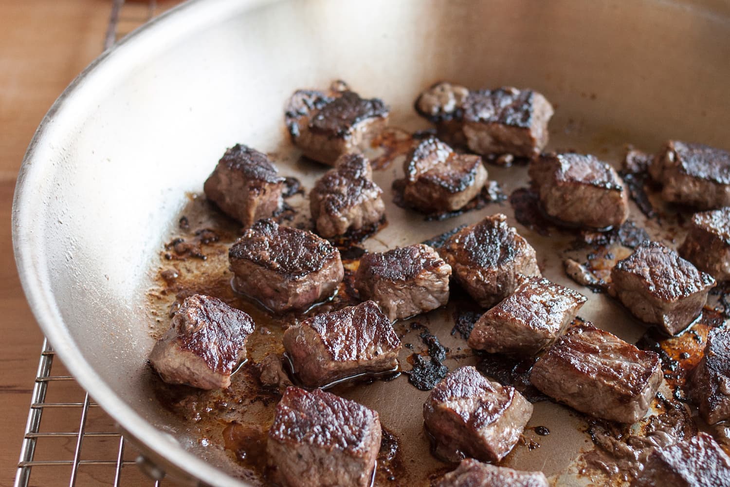 Browned beef cubes resting on a plate beside a Dutch oven with browned bits on the bottom