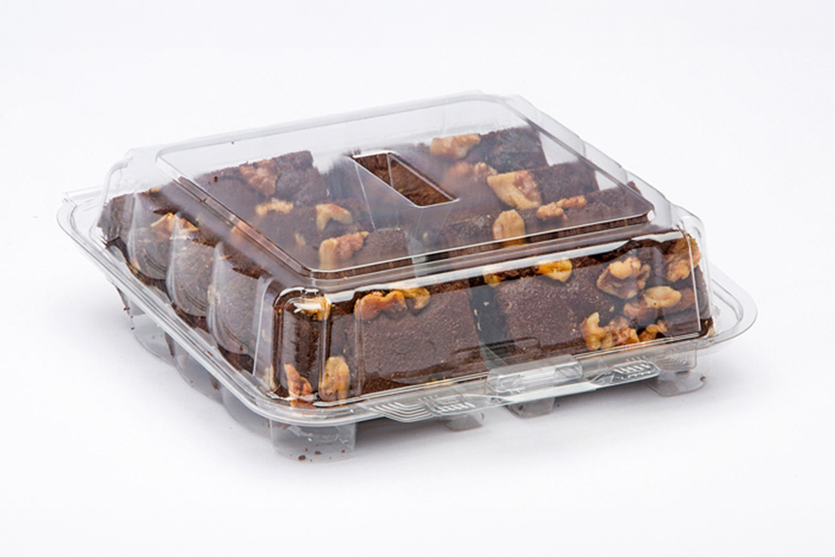Brownie squares wrapped and stacked inside a glass storage container on a kitchen counter