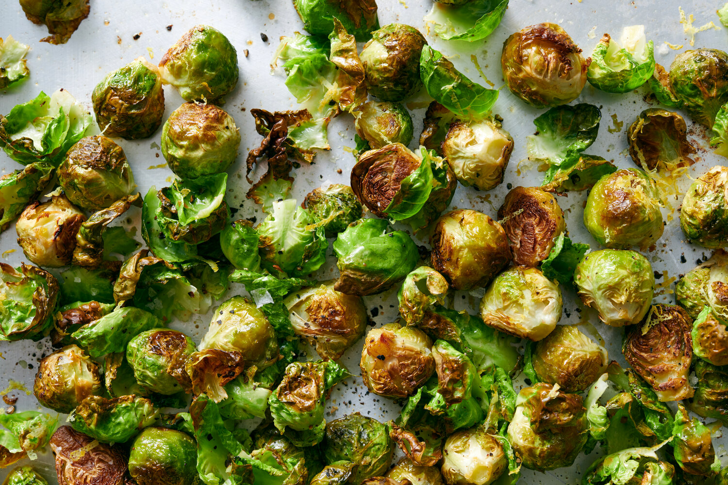 Brussels sprouts, olive oil, garlic, a lemon, salt, pepper, and grated Parmesan arranged on a kitchen counter
