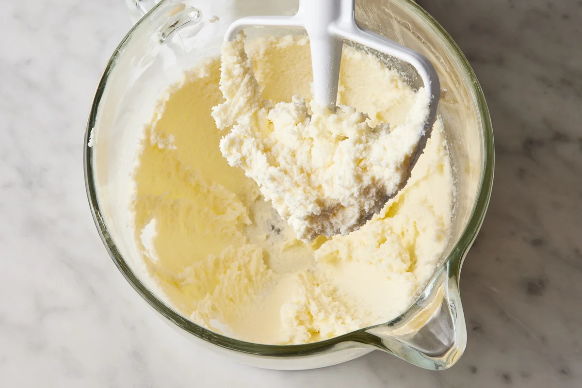 Butter and brown sugar being creamed together in a mixing bowl with a hand mixer on a kitchen counter