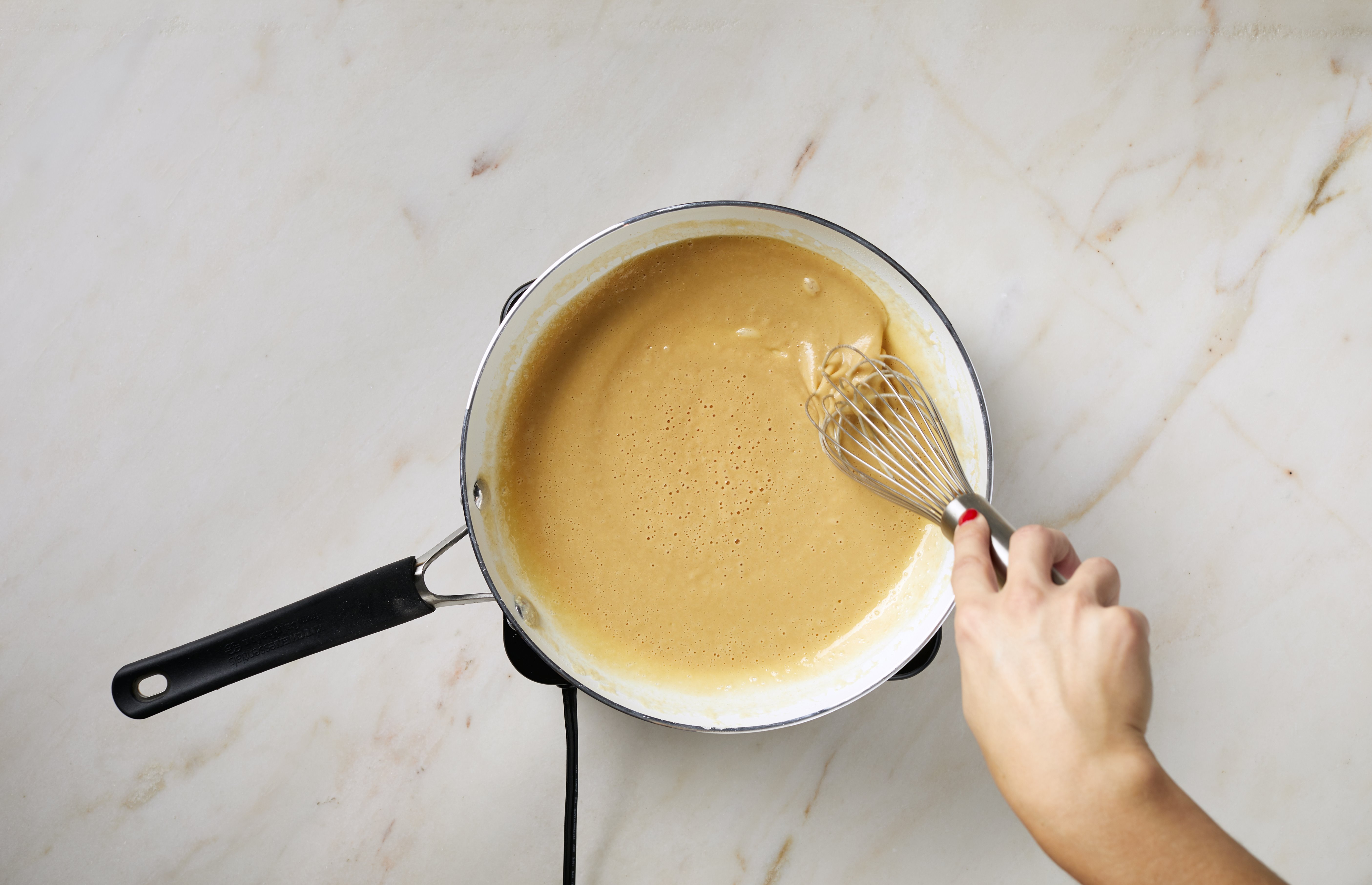 Butter and flour roux being whisked in a saucepan on a stove, early stage of cheese sauce