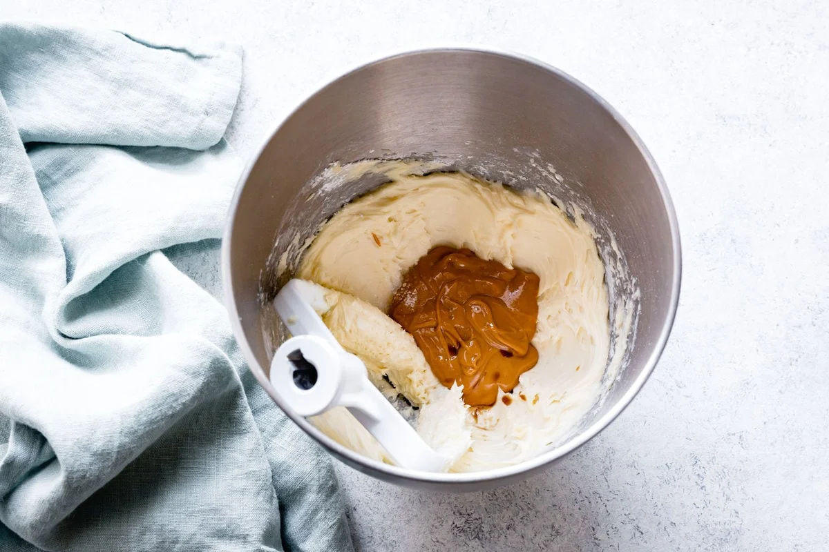 Butter and peanut butter being beaten together with a mixer in a bowl, mid-whip with a smooth creamy texture