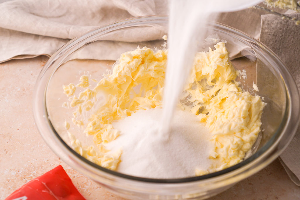 Butter and powdered sugar being creamed together in a mixing bowl with a hand mixer on a kitchen counter