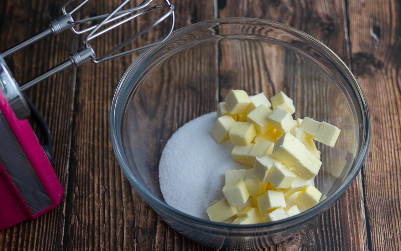 Butter and sugar being creamed in a mixing bowl until pale and fluffy on a kitchen counter