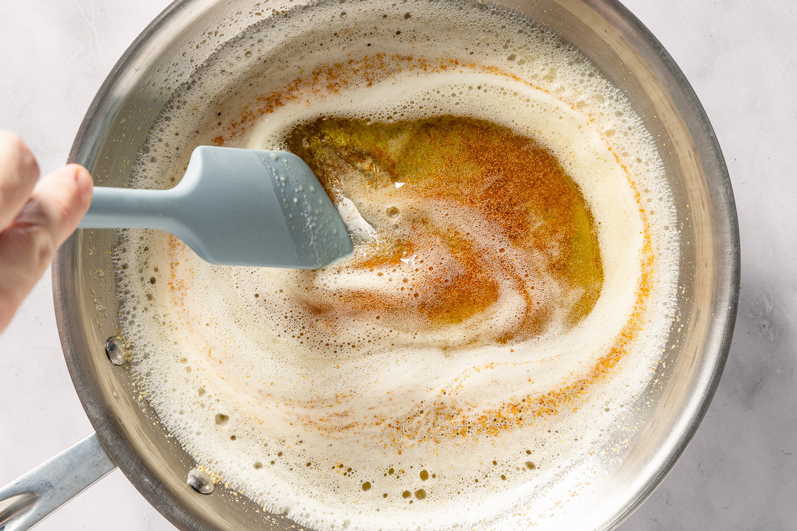 Butter foaming and browning in a light-colored saucepan on a stovetop, with toasted milk solids visible at the bottom