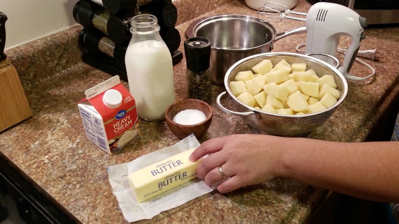 Butter, heavy cream, milk, kosher salt, black pepper, and peeled potato chunks arranged on a tidy kitchen counter
