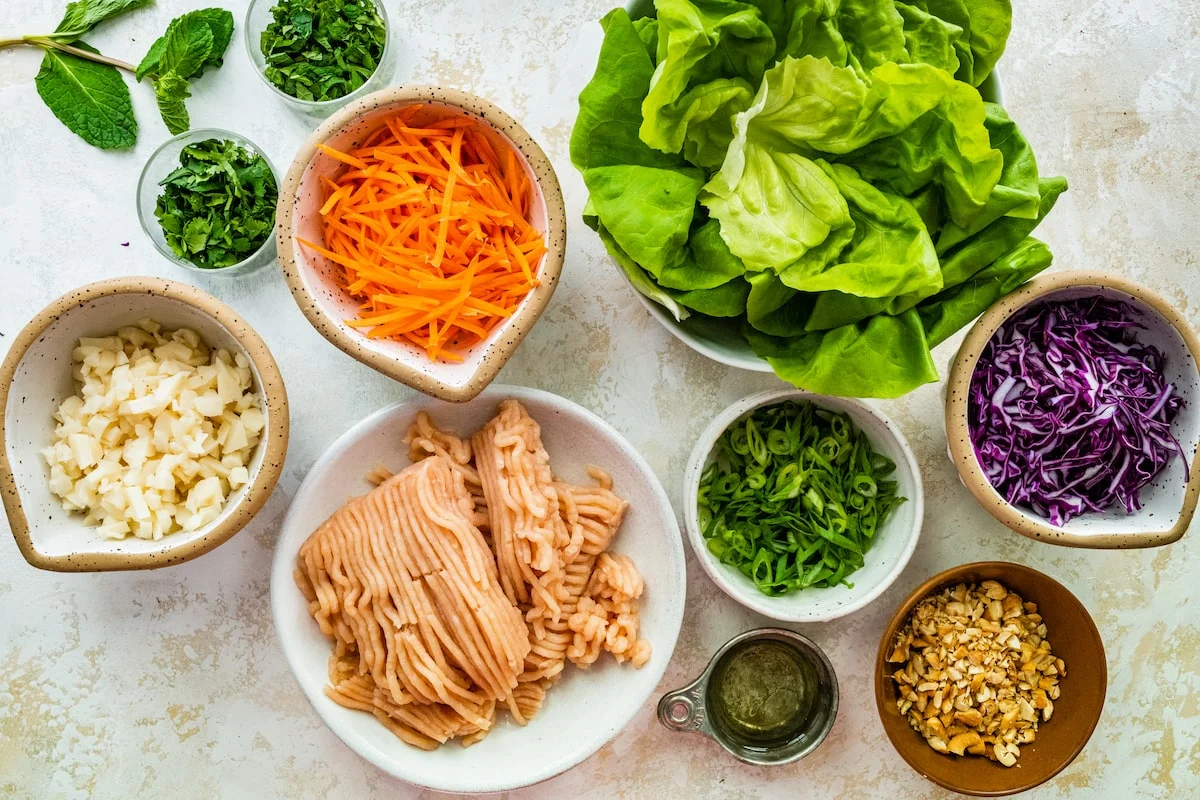 Butter lettuce, ground chicken, water chestnuts, mushrooms, green onions, garlic, ginger, soy sauce, hoisin sauce, and rice vinegar arranged on a bright kitchen counter
