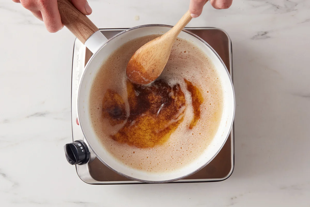 Butter melting and browning in a small stainless steel saucepan on a stovetop, with golden milk solids visible at the bottom