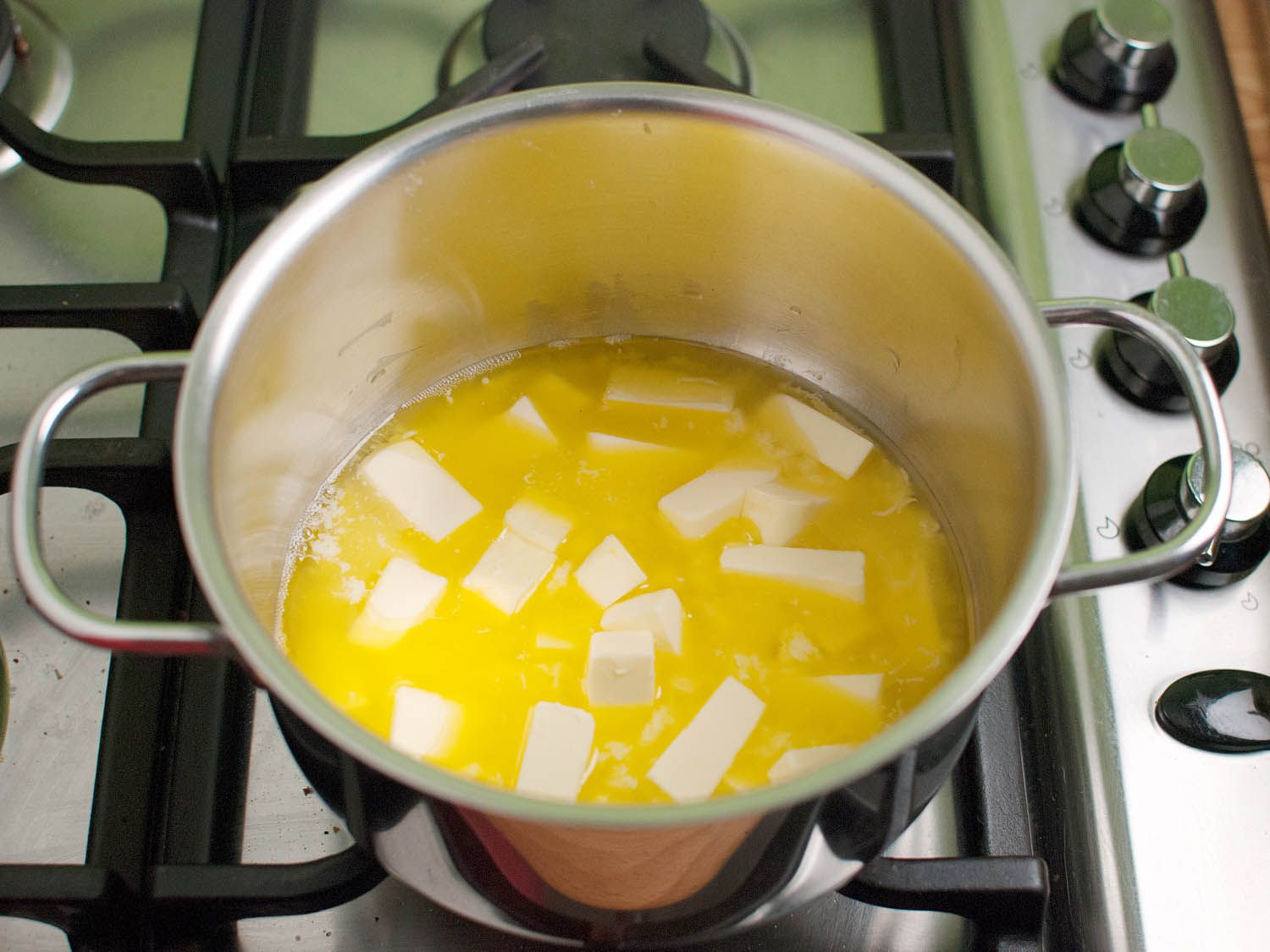 Butter melting in a small saucepan on a stovetop with a wooden spoon nearby in a home kitchen