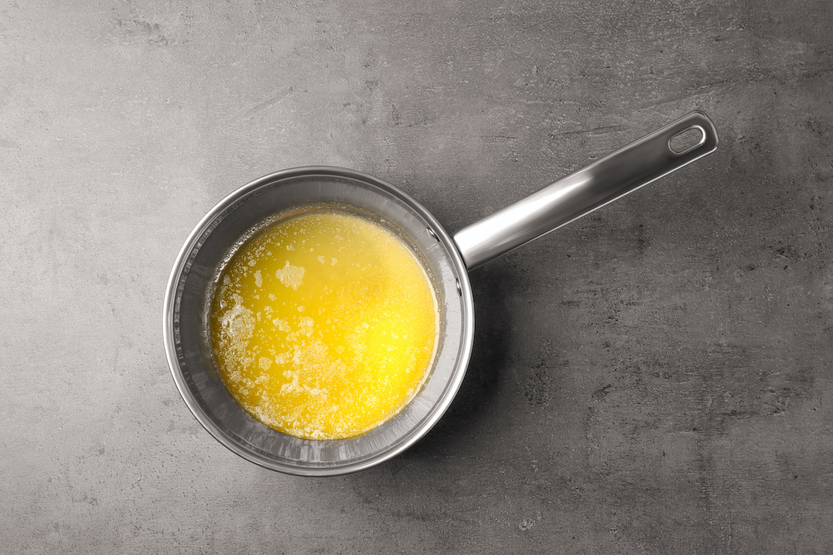 Butter melting in a stainless steel saucepan on a stovetop burner, with a wooden spoon resting nearby