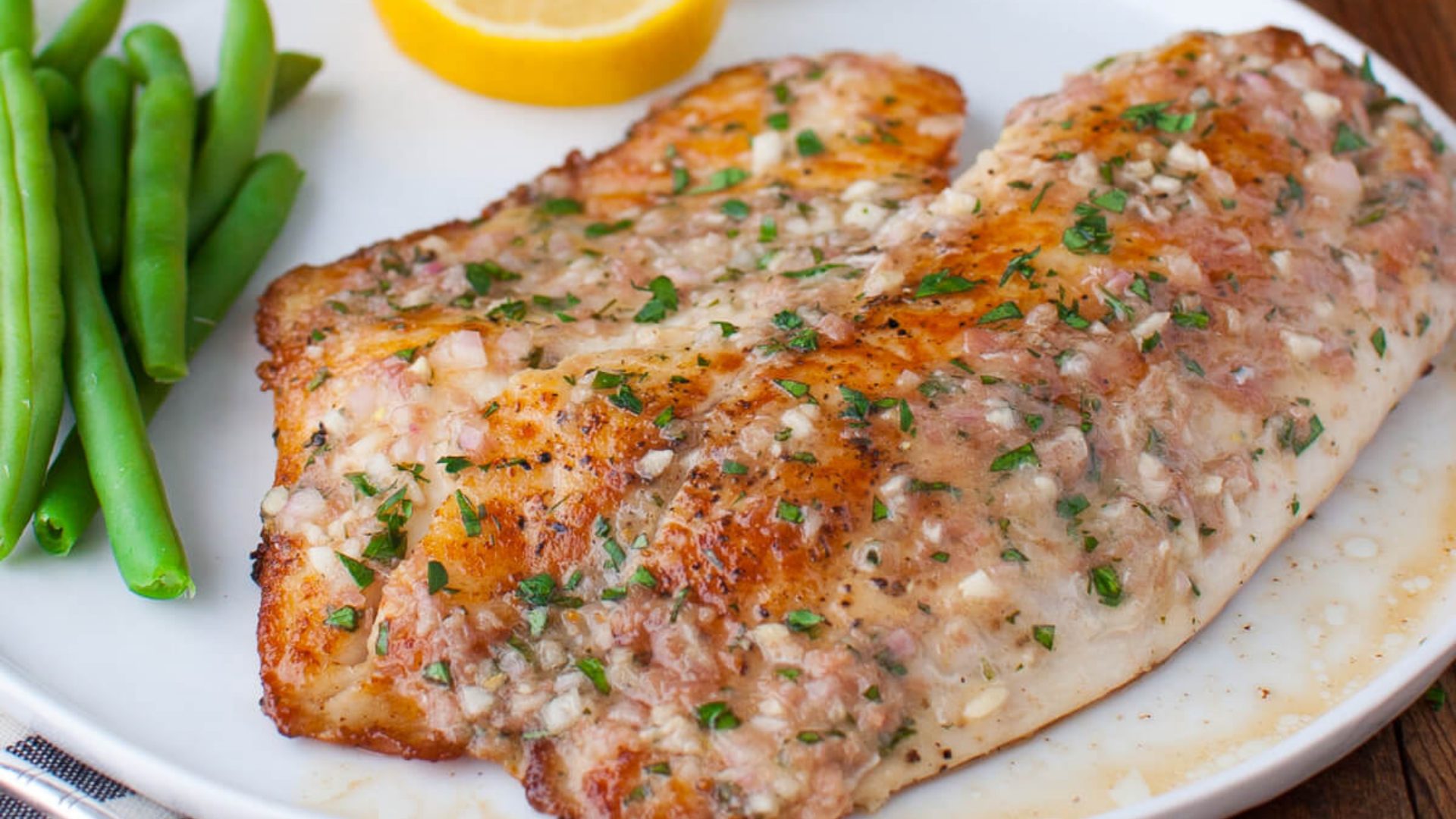 Butter, minced garlic, lemon, parsley, paprika, salt, pepper, and raw tilapia fillets arranged on a light kitchen counter with measuring spoons
