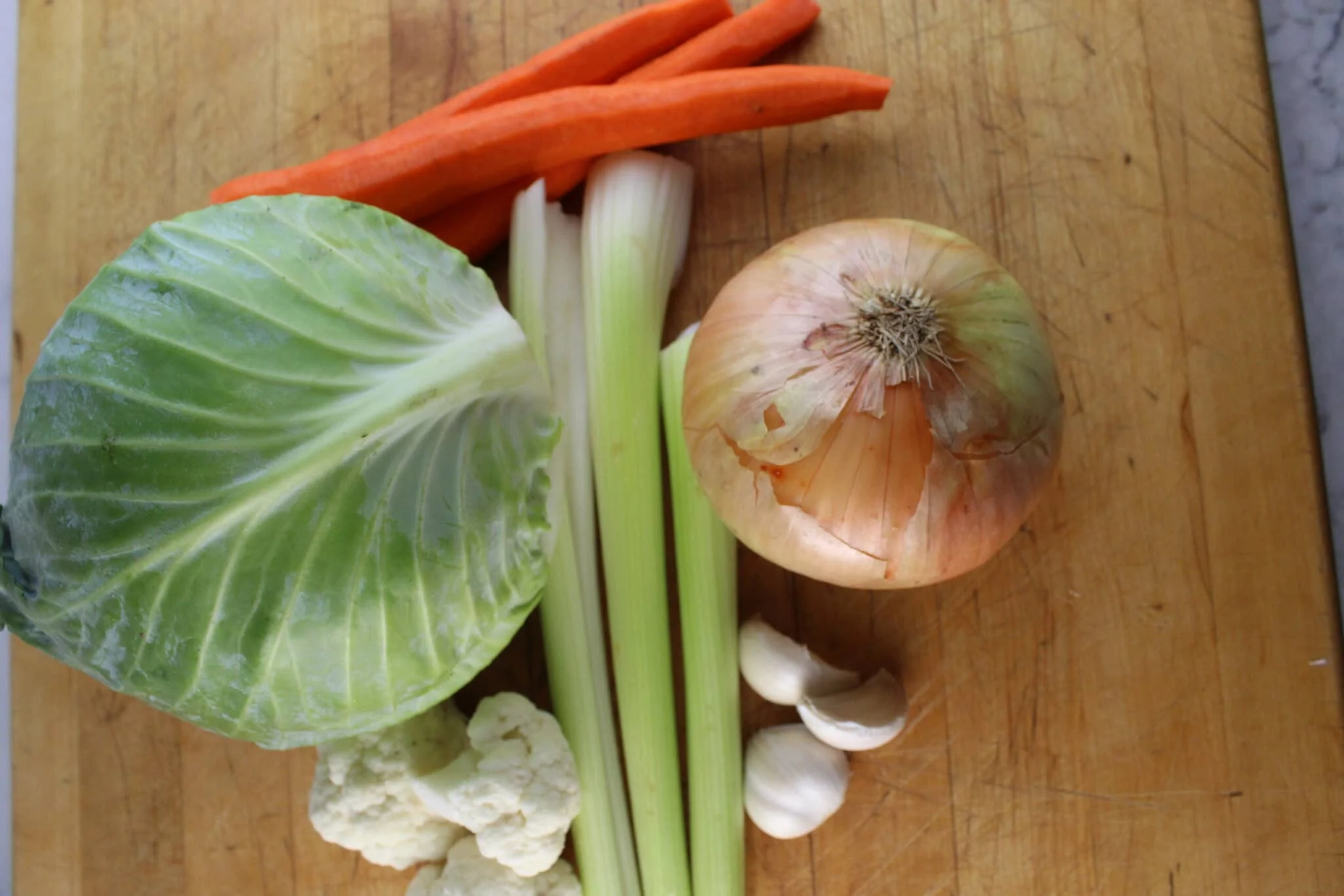 Cabbage, carrots, celery, onion, garlic, canned tomatoes, and broth arranged on a kitchen counter