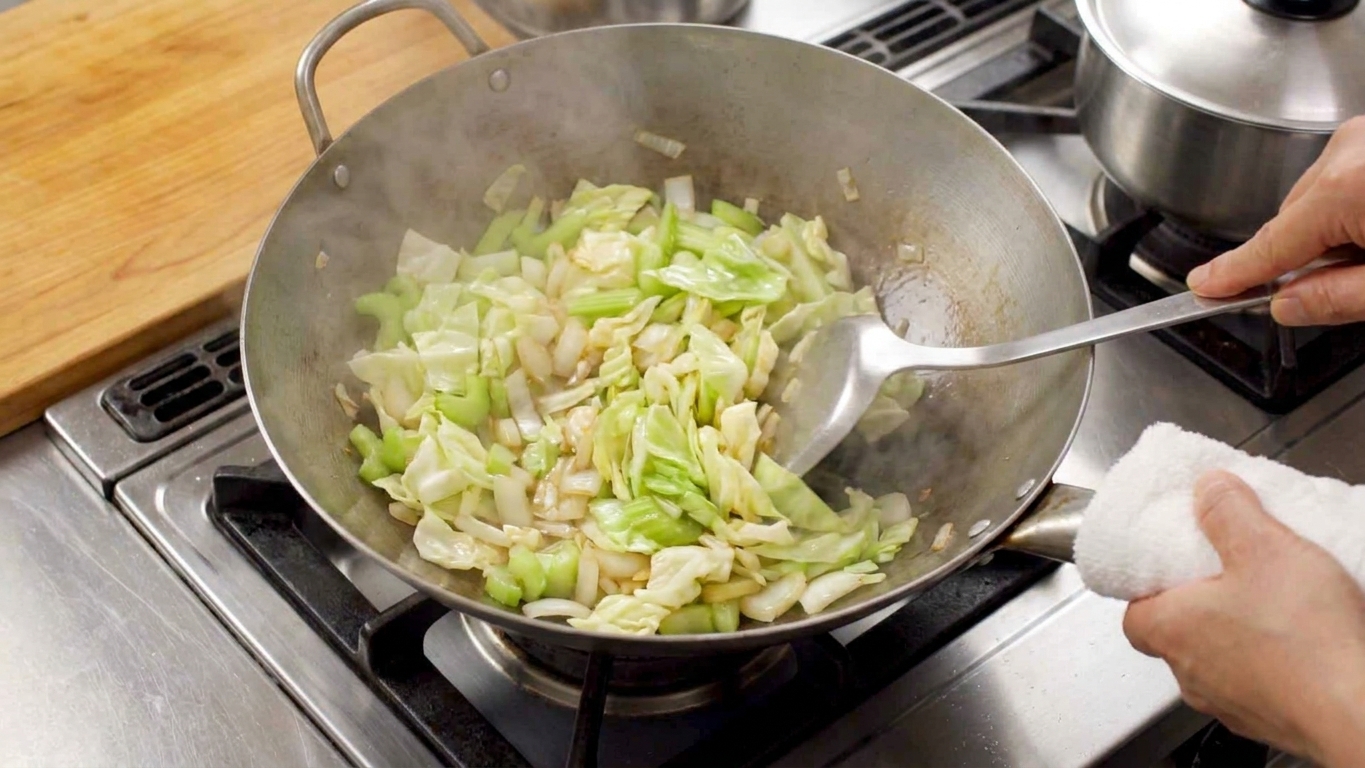 Cabbage, celery, and onion being stir-fried in a wok on a stovetop