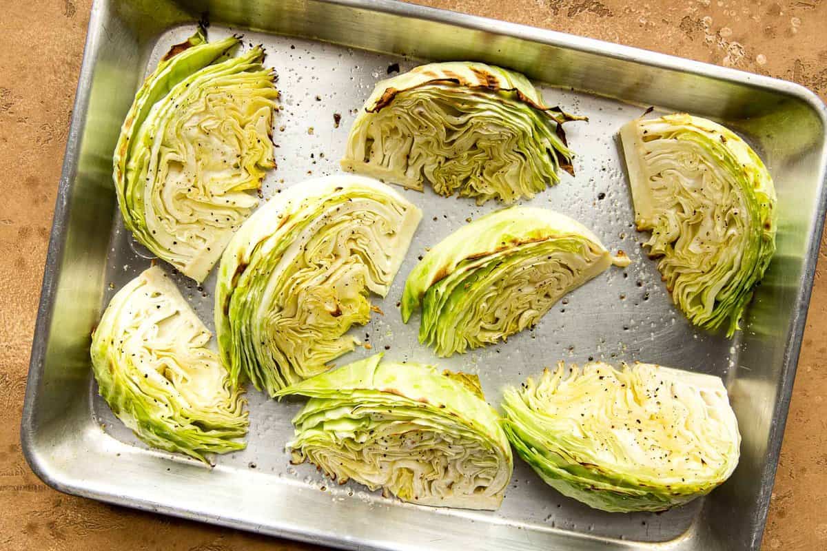 Cabbage wedges arranged cut-side down on a hot sheet pan in an oven, beginning to brown at the edges