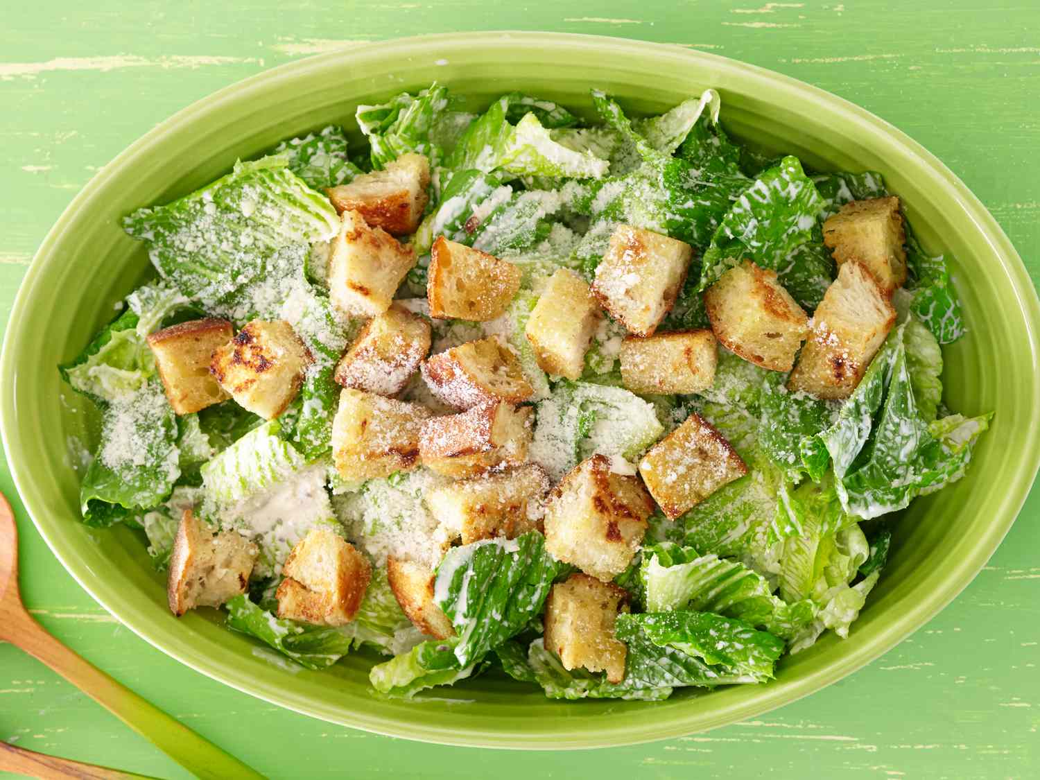 Caesar salad ingredients arranged on a kitchen counter including romaine hearts, Parmesan, lemon, garlic, anchovies, Dijon mustard, eggs, olive oil, bread, and chicken breasts