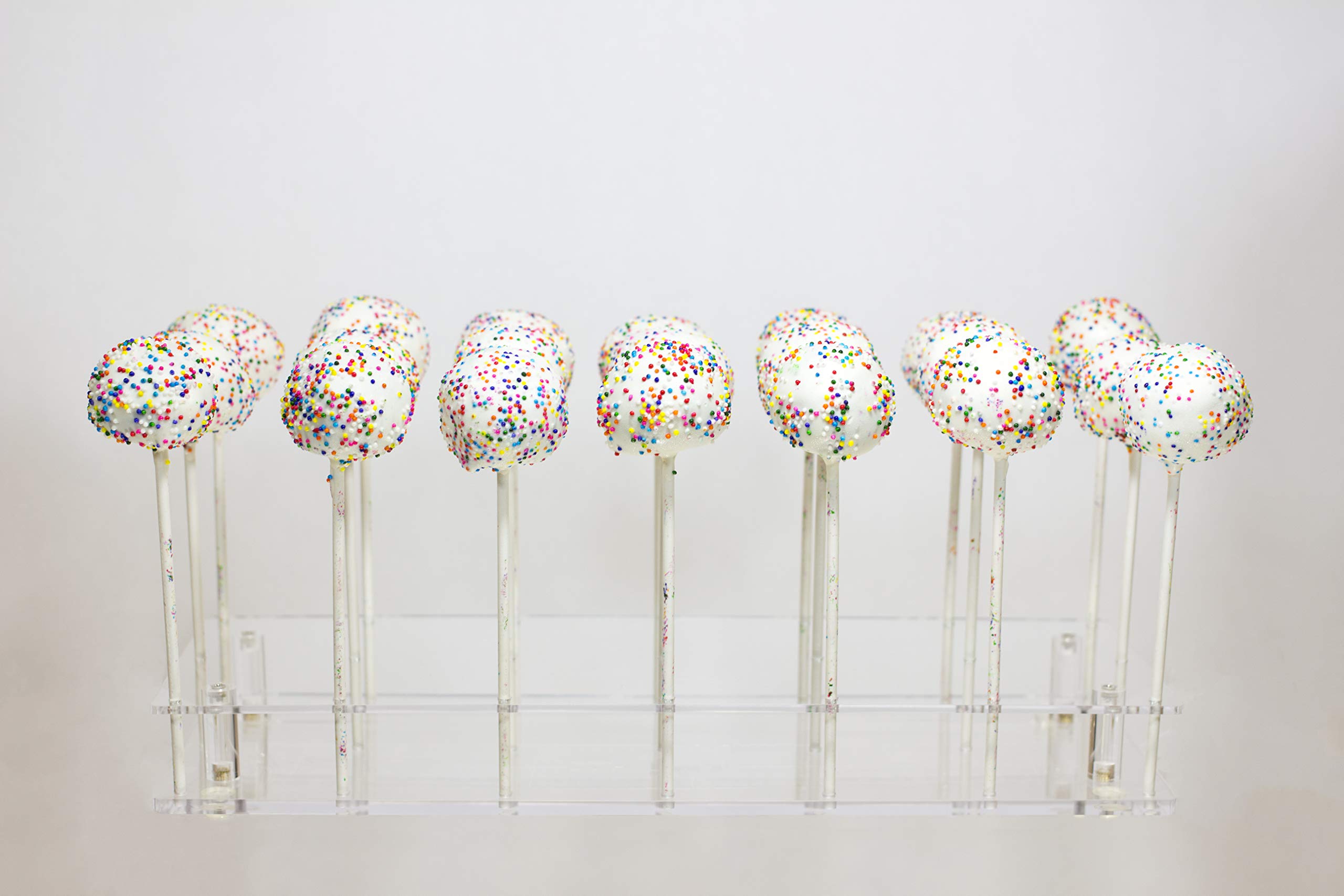 Cake pops standing upright in a foam block on a kitchen counter, with parchment paper underneath to catch drips