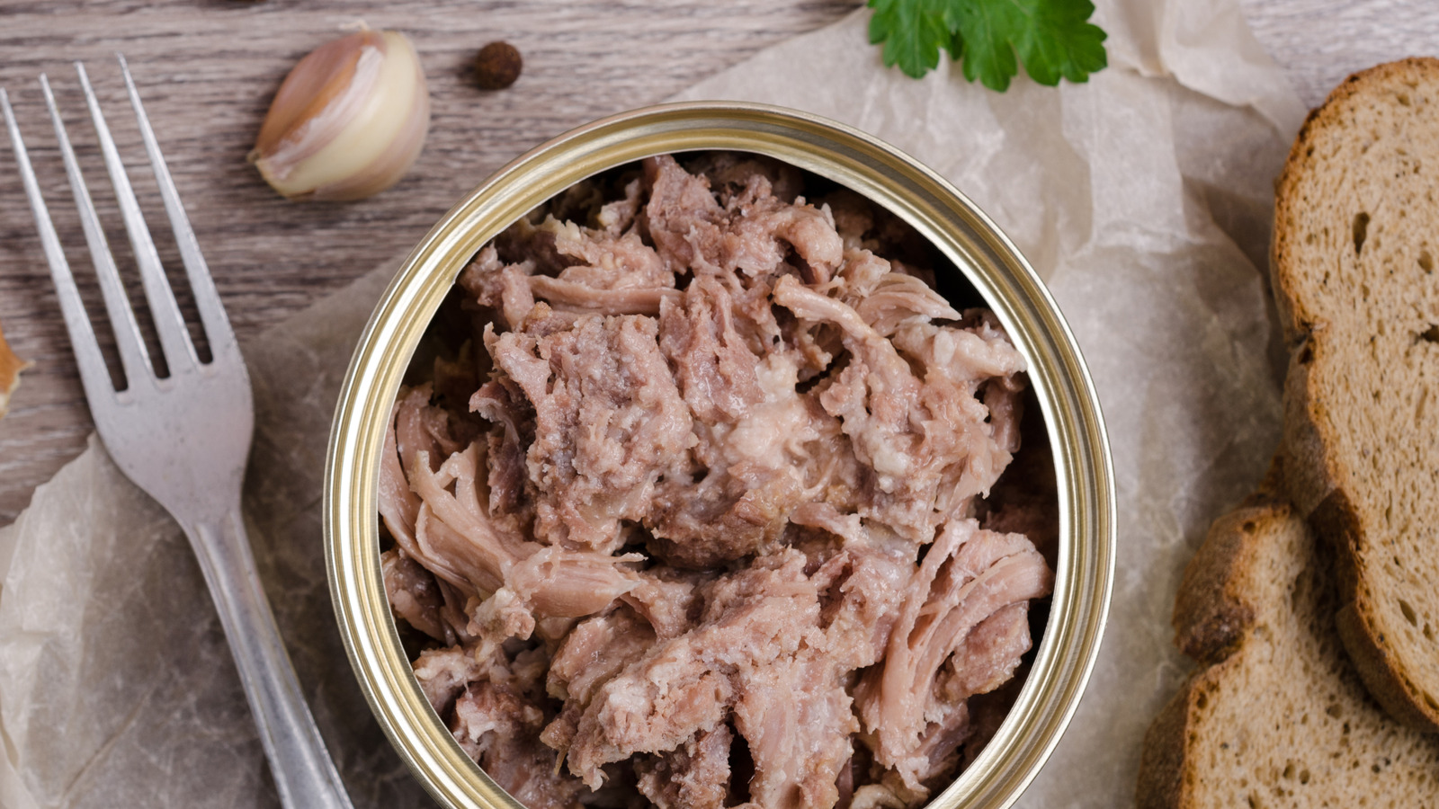 Canned chicken being pressed and drained in a fine mesh strainer over a sink on a home kitchen counter