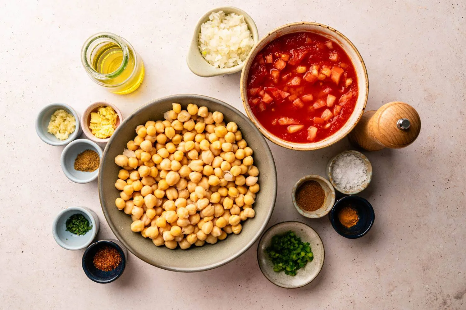 Canned chickpeas, olive oil, lemon, garlic, yogurt, and small bowls of spices arranged on a tidy kitchen counter in natural light