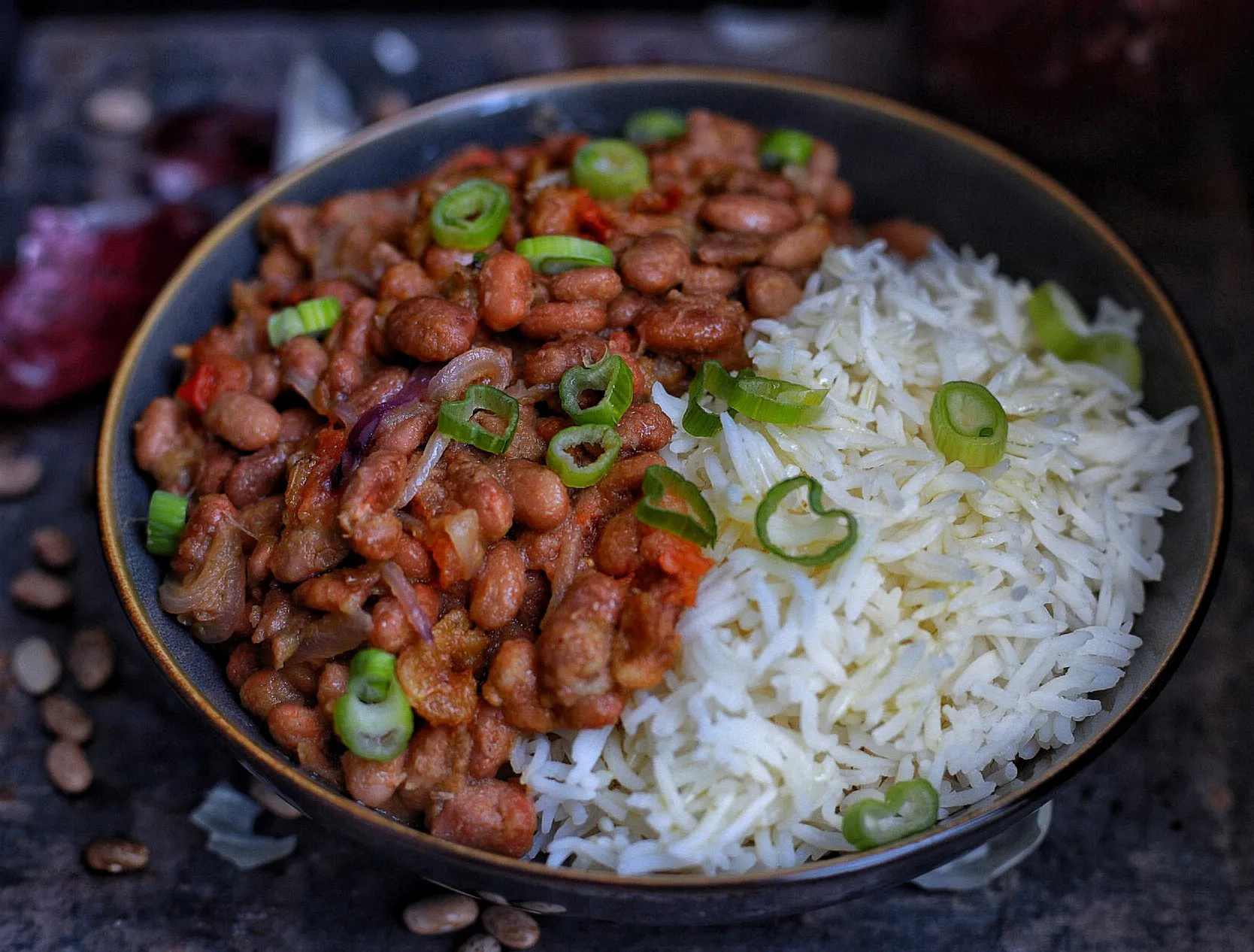 Canned pinto beans, uncooked rice, onion, garlic, lime, and spices laid out on a tidy kitchen counter with warm natural light
