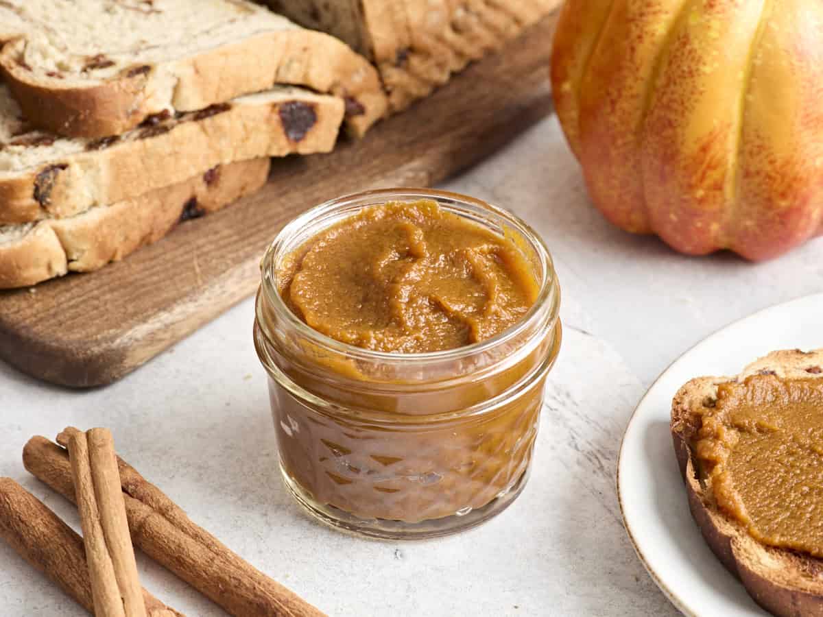Canned pumpkin, maple syrup, apple cider, brown sugar, and small bowls of spices arranged on a bright kitchen counter with warm natural light