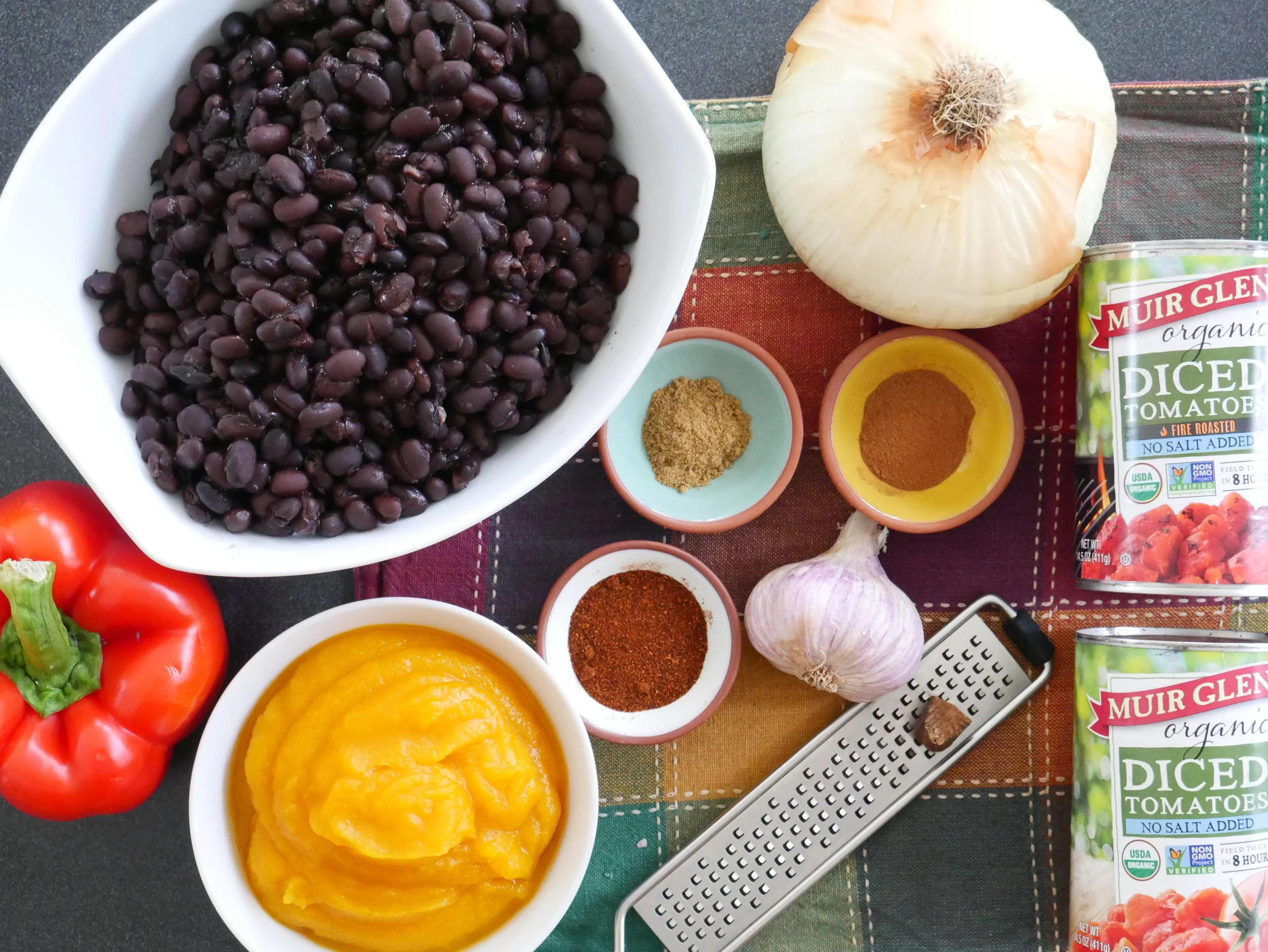 Canned pumpkin puree, ground meat, beans, diced tomatoes, onions, garlic, and spices arranged on a clean kitchen counter ready for cooking