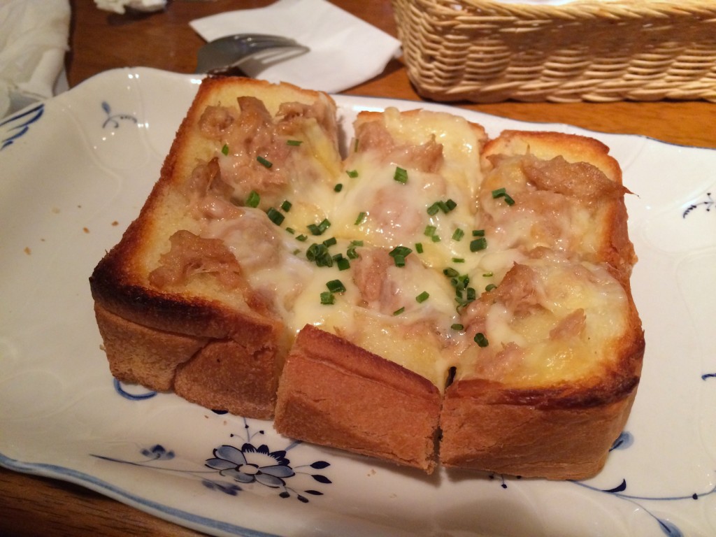 Canned tuna, a measuring cup of milk, flour, butter, salt, pepper, and bread laid out on a clean kitchen counter with warm natural light