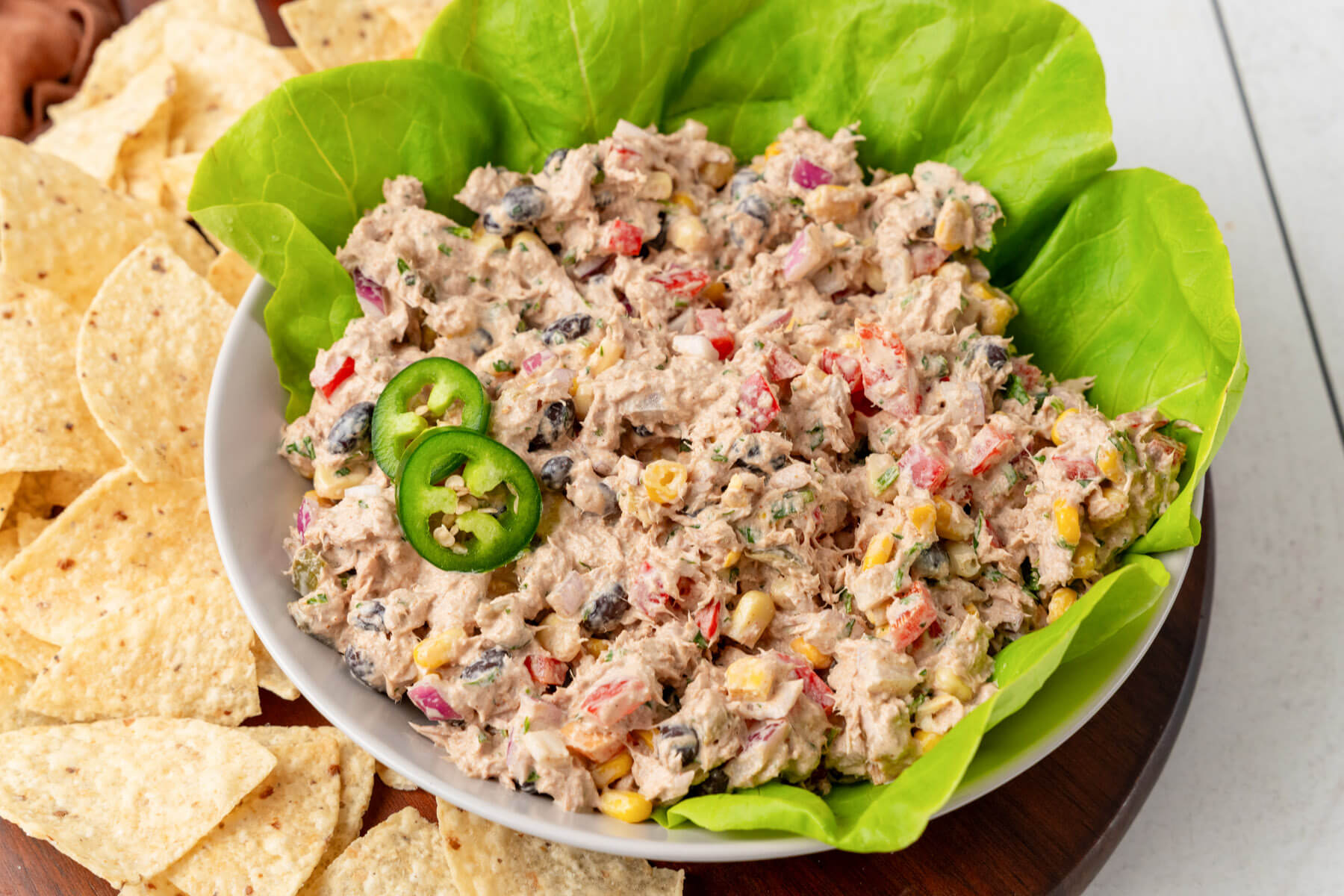 Canned tuna, mayonnaise, Dijon mustard, lemons, celery, cucumber, red onion, capers, salt, pepper, and fresh parsley arranged on a bright kitchen counter