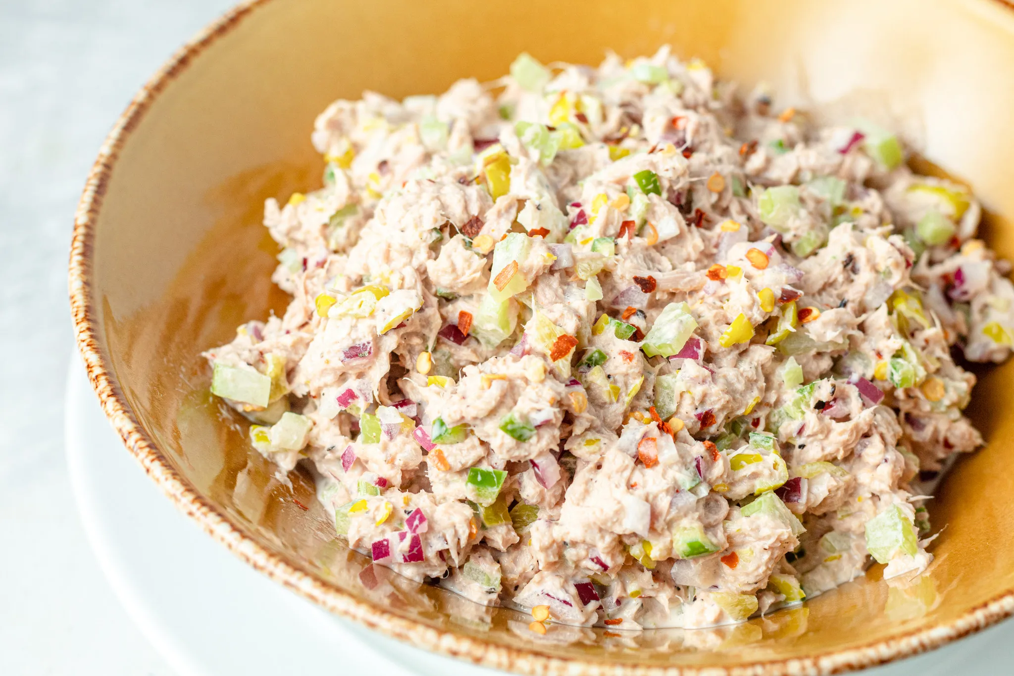 Canned tuna, mayonnaise, lemon, Dijon mustard, chopped celery, chopped pickles, red onion, and seasonings arranged on a clean kitchen counter in bright natural light