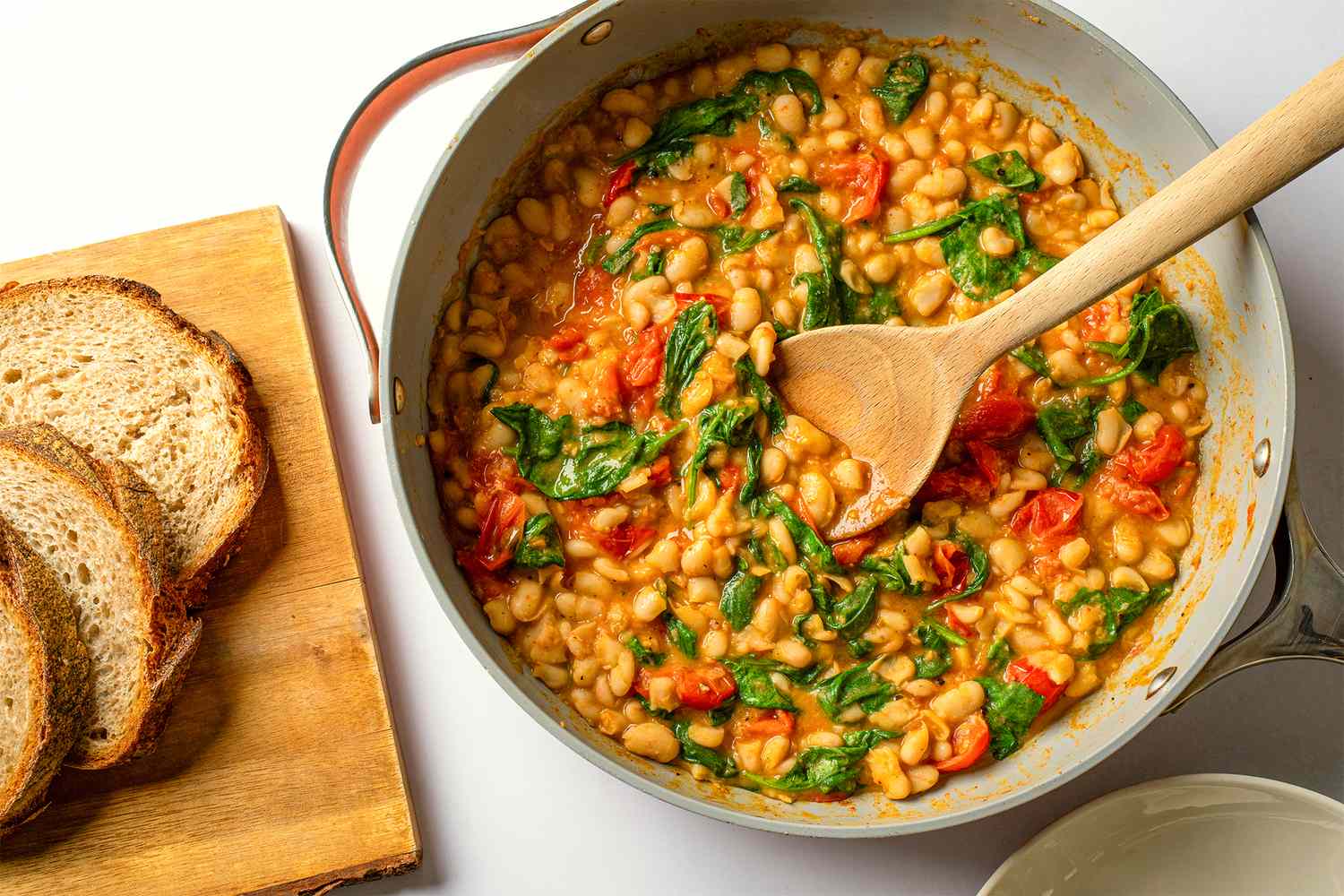 Canned white beans, cherry tomatoes, fresh spinach, garlic, lemon, and basil arranged on a wooden cutting board on a bright kitchen counter