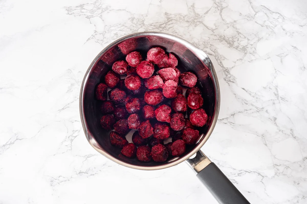 Cherries and sugar mixed together in a stainless steel saucepan before cooking