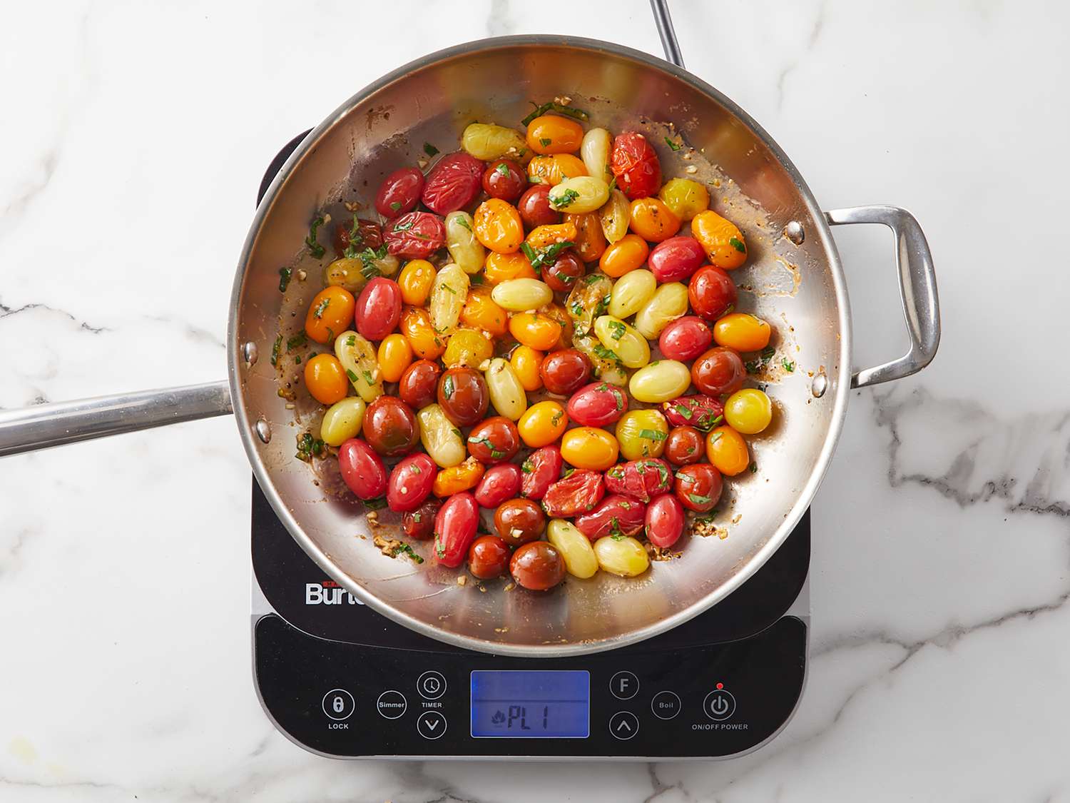 Cherry tomatoes, garlic cloves, fresh basil, lemon, and olive oil arranged on a wooden cutting board on a bright kitchen counter