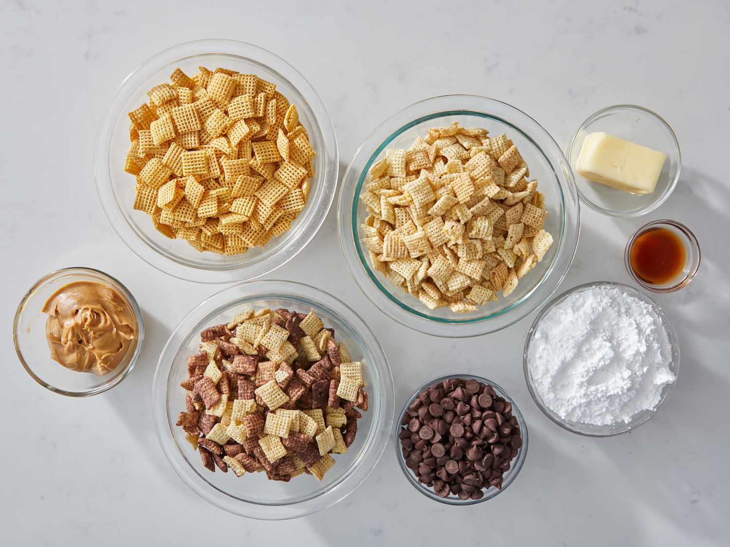 Chex cereal, chocolate chips, peanut butter, powdered sugar, and vanilla arranged on a clean kitchen counter with measuring cups nearby