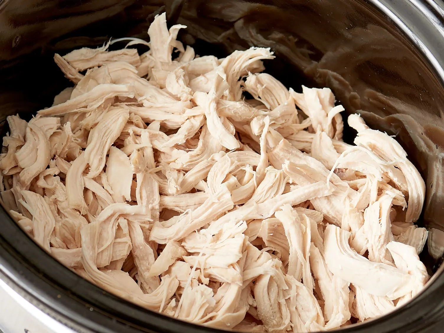 Chicken breasts, chicken broth, olive oil, and small bowls of spices arranged on a kitchen counter beside a slow cooker