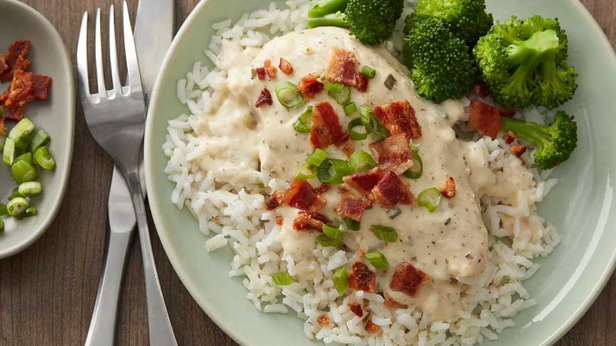 Chicken breasts in a slow cooker with cubes of cream cheese and ranch seasoning sprinkled on top before cooking
