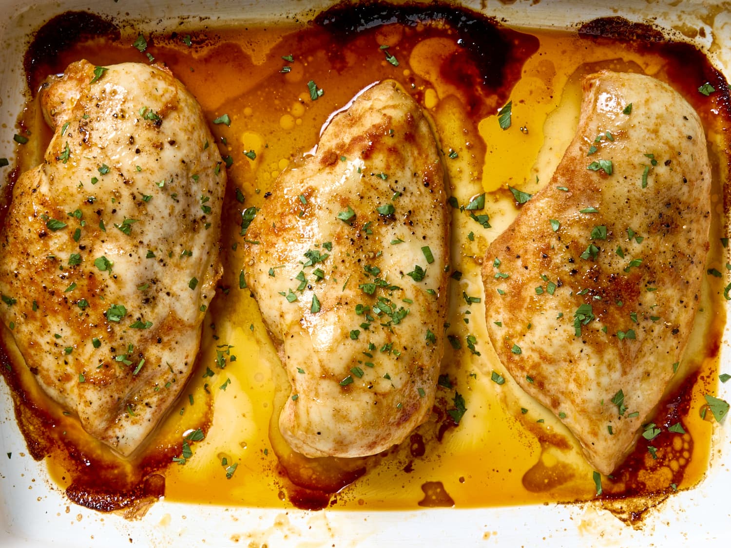 Chicken breasts on a cutting board being seasoned with salt, pepper, garlic powder, and Italian seasoning next to small bowls of spices