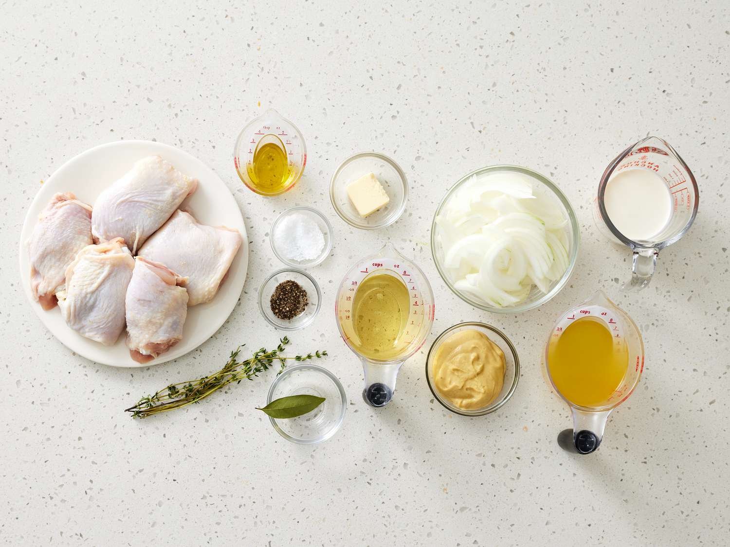 Chicken cutlets, Dijon mustard, heavy cream, chicken broth, garlic, lemon, butter, and herbs arranged on a kitchen counter with measuring spoons