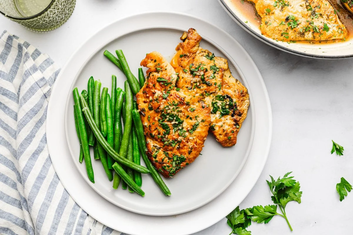 Chicken cutlets searing in a hot skillet with golden-brown edges forming