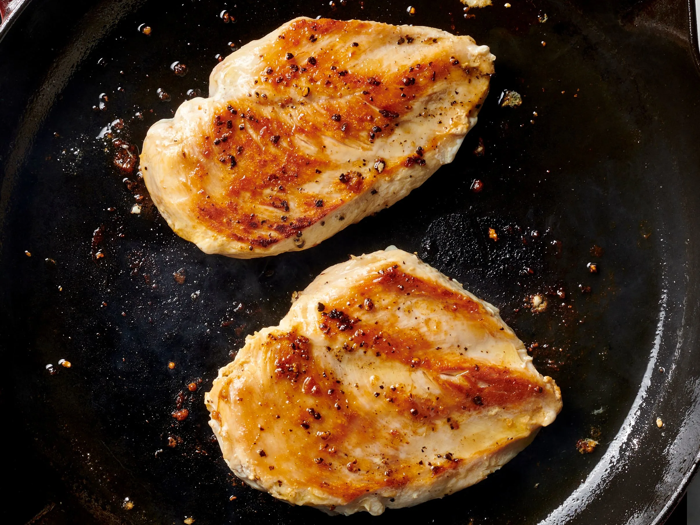 Chicken cutlets searing in a hot skillet with golden brown edges forming