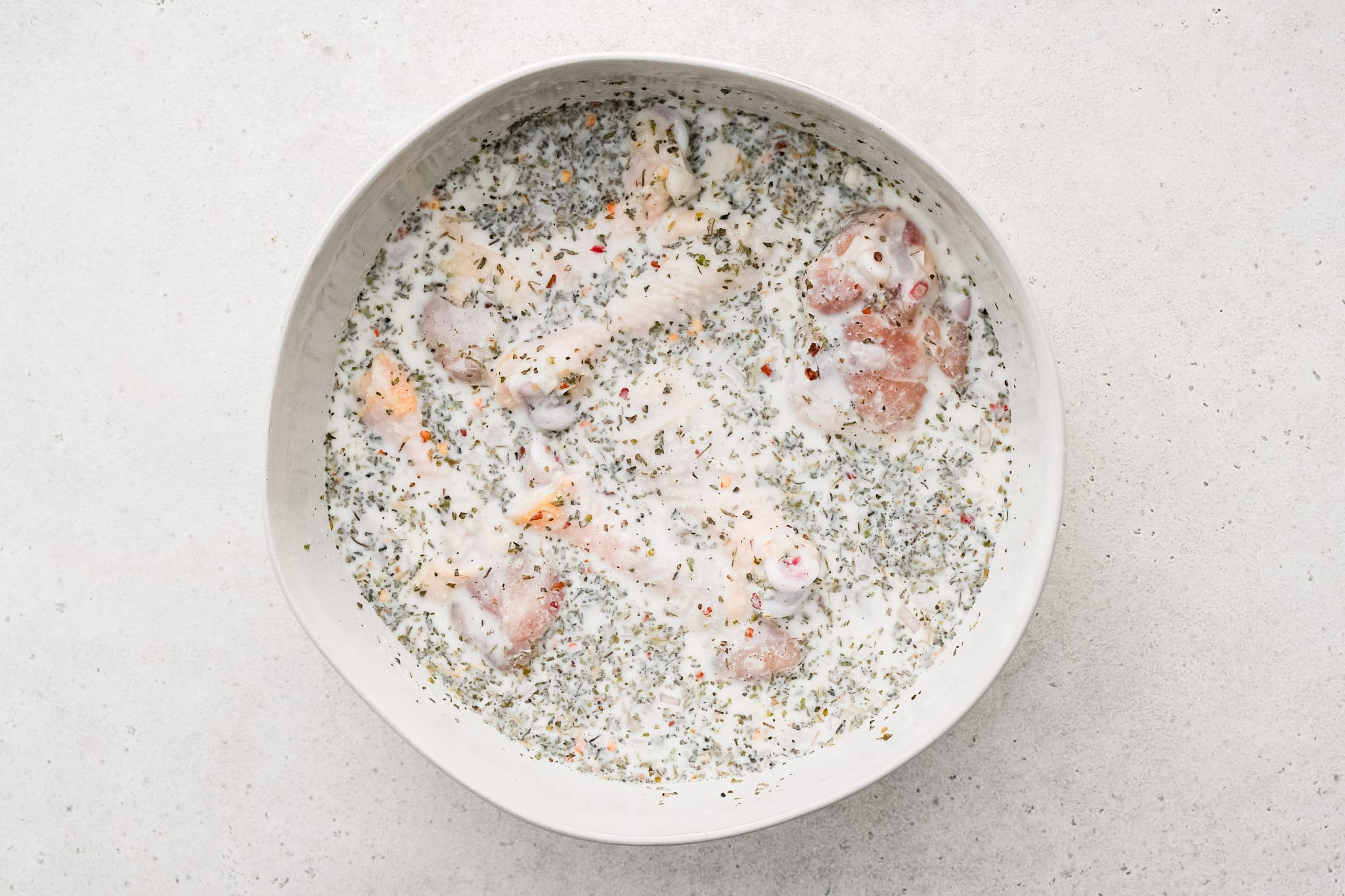 Chicken cutlets soaking in a bowl of seasoned buttermilk marinade on a kitchen counter