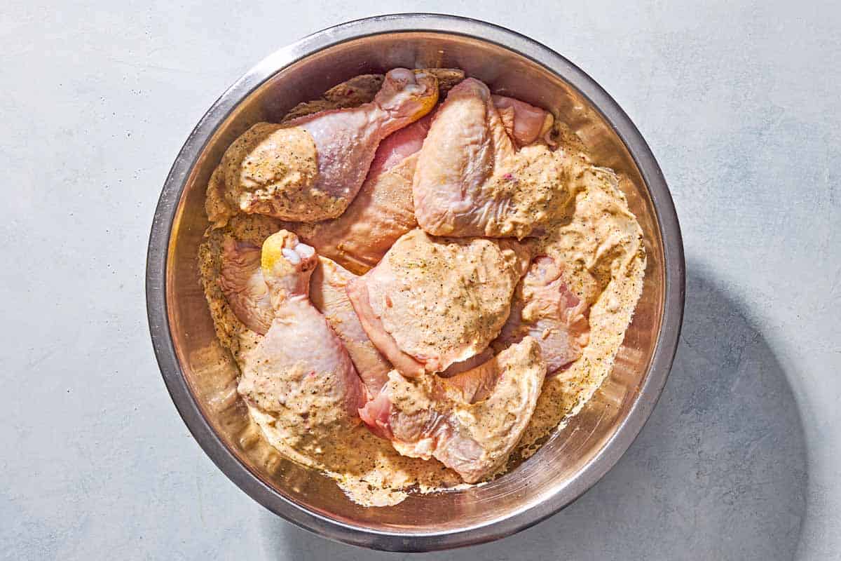 Chicken pieces coated in a creamy yogurt lemon marinade in a mixing bowl with a spoon, sitting on a kitchen counter