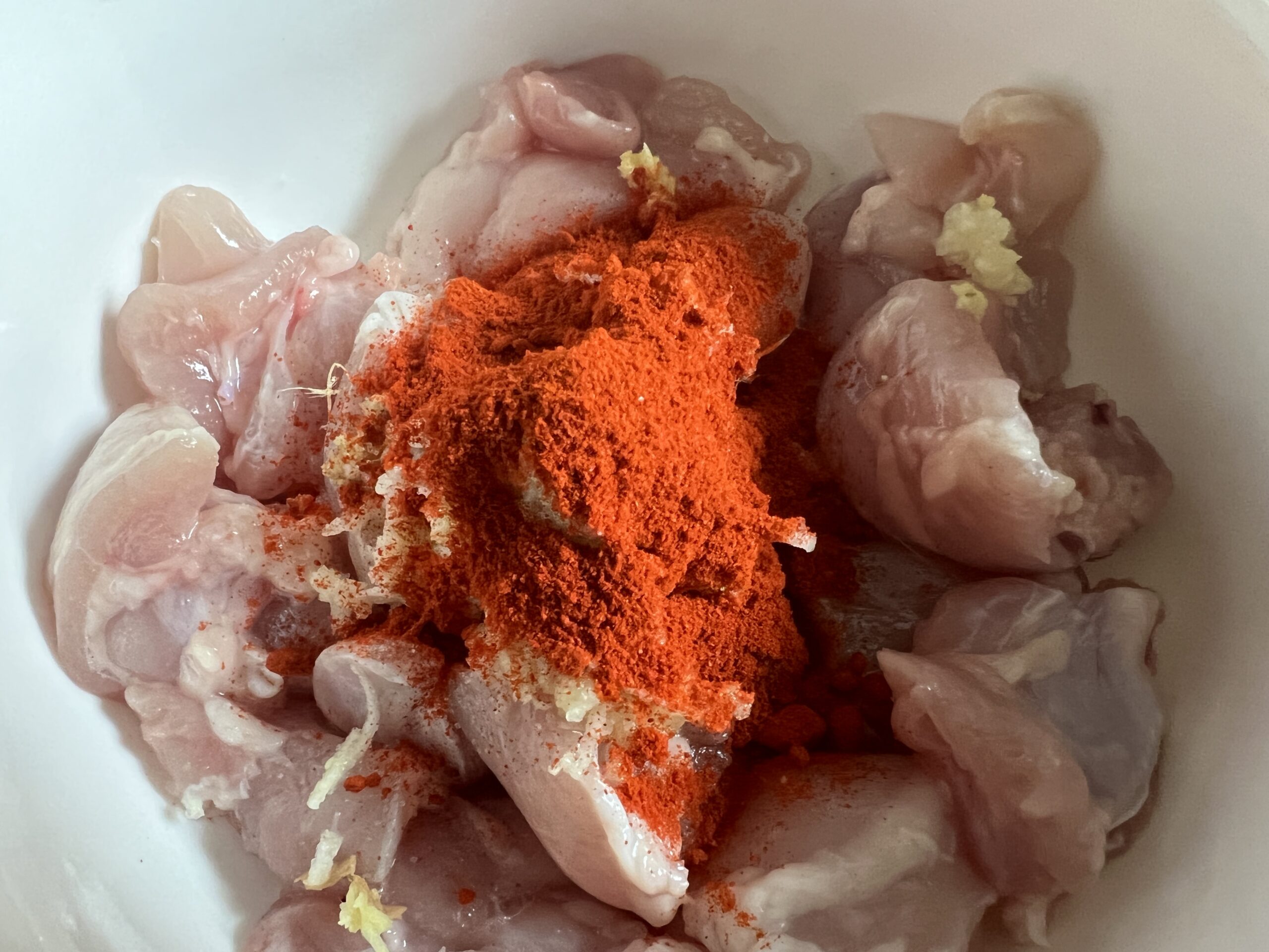 Chicken pieces coated in a reddish yogurt marinade being stirred in a mixing bowl on a kitchen counter