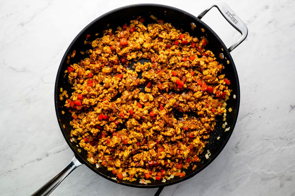 Chicken pieces cooking in a skillet coated in smoky taco seasoning with a wooden spoon stirring on a stovetop