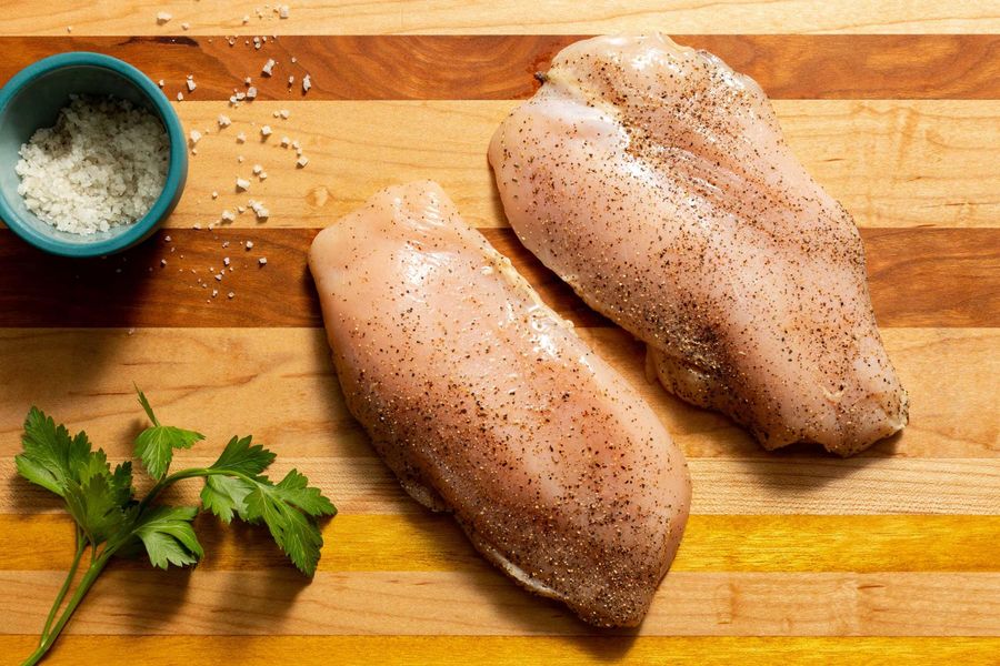 Chicken pieces patted dry and seasoned with salt and pepper on a cutting board, ready to cook