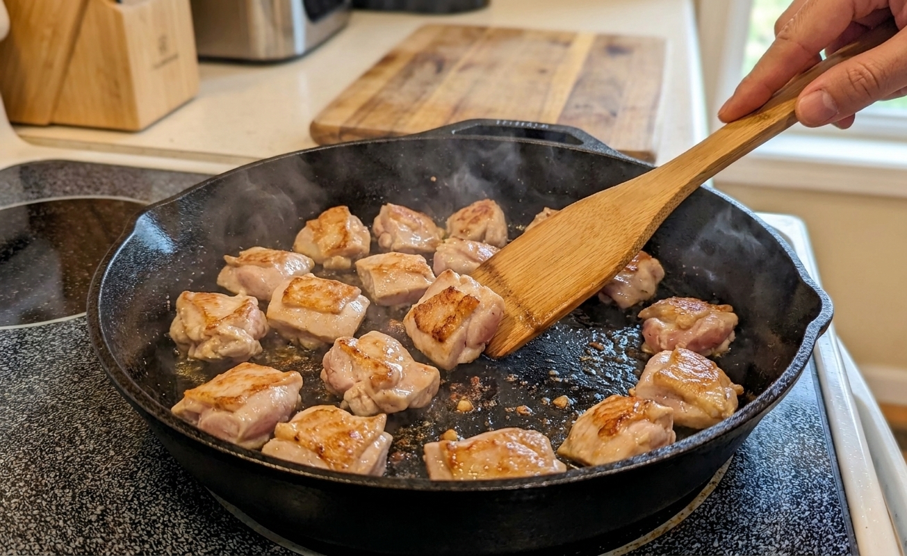 Chicken pieces sizzling in a hot skillet with golden edges forming on a home stove