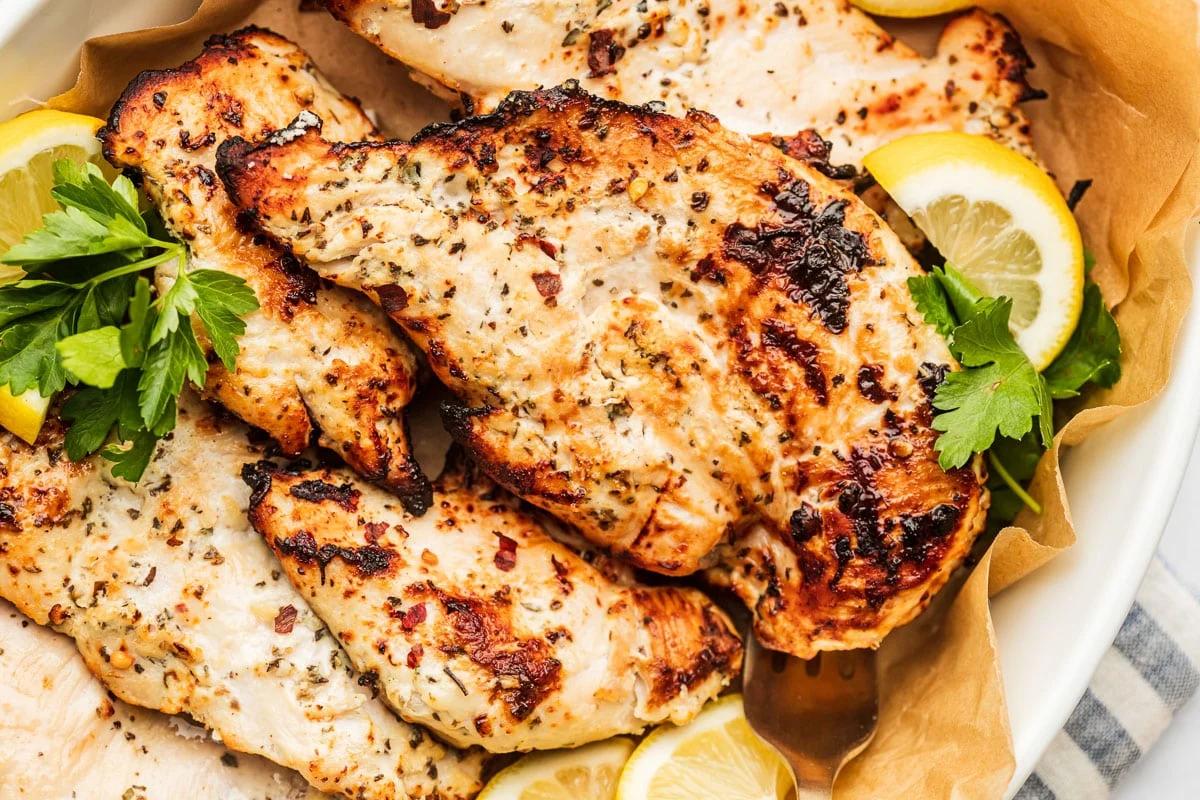 Chicken thigh pieces in a glass bowl coated in a pale yogurt spice marinade on a clean kitchen counter