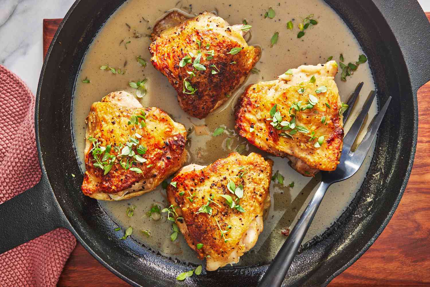 Chicken thighs browning in a hot skillet with golden brown edges forming, tongs resting on the pan rim in a home kitchen