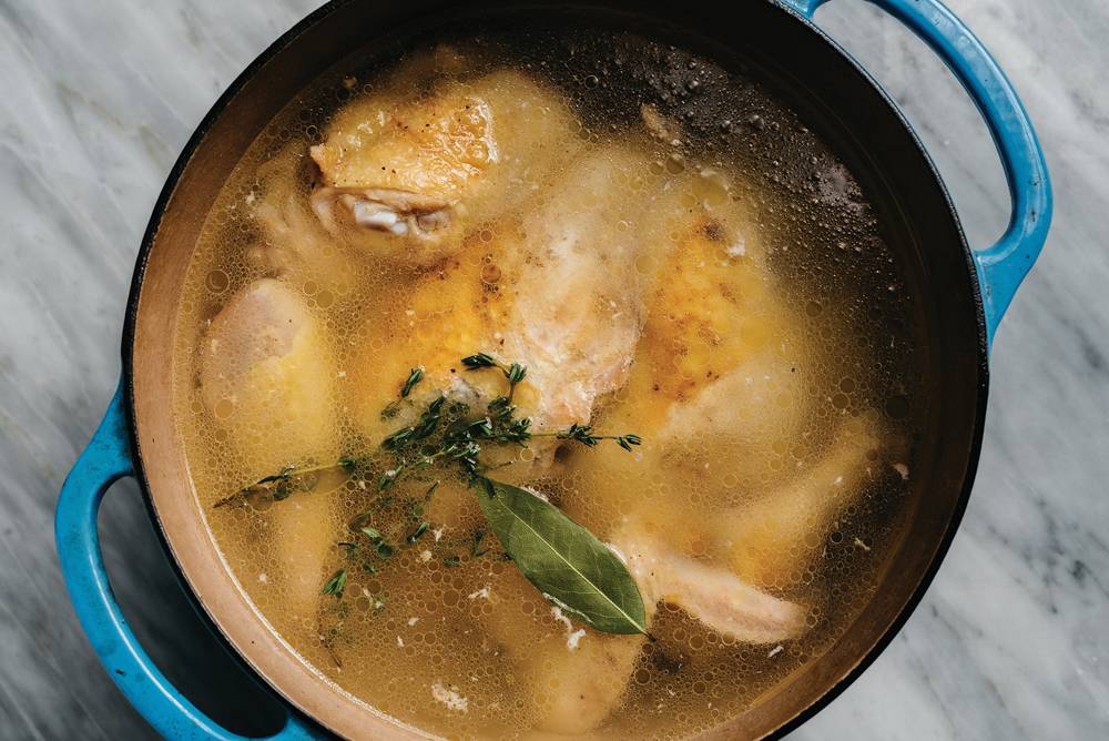 Chicken thighs gently simmering in broth with vegetables and herbs in a large pot