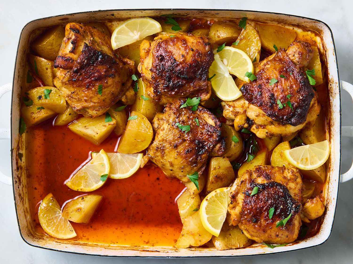 Chicken thighs, halved baby potatoes, lemon, garlic, broth, butter, and herbs measured and ready on a kitchen counter